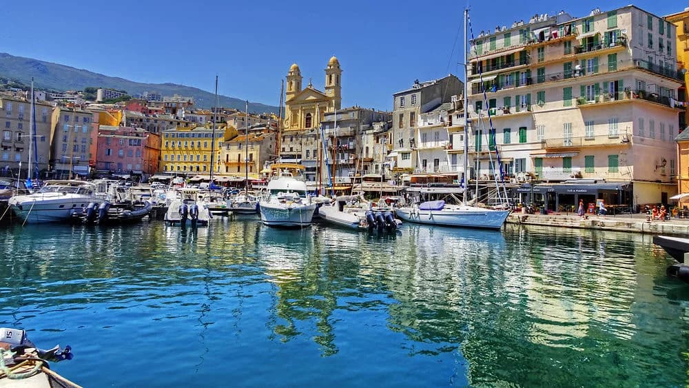 Le Vieux-Port de Bastia, ses façades colorées et l’église Saint-Jean-Baptiste se reflètent dans la mer.